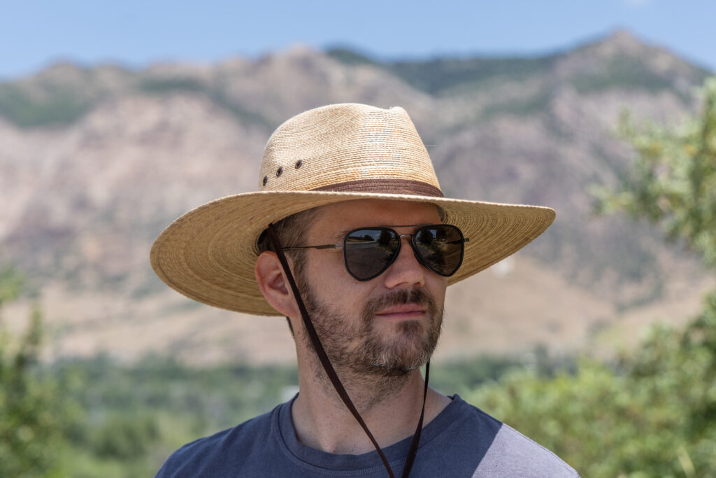 A man stands in front of mountains in a Wallaroo Baja sun hat.