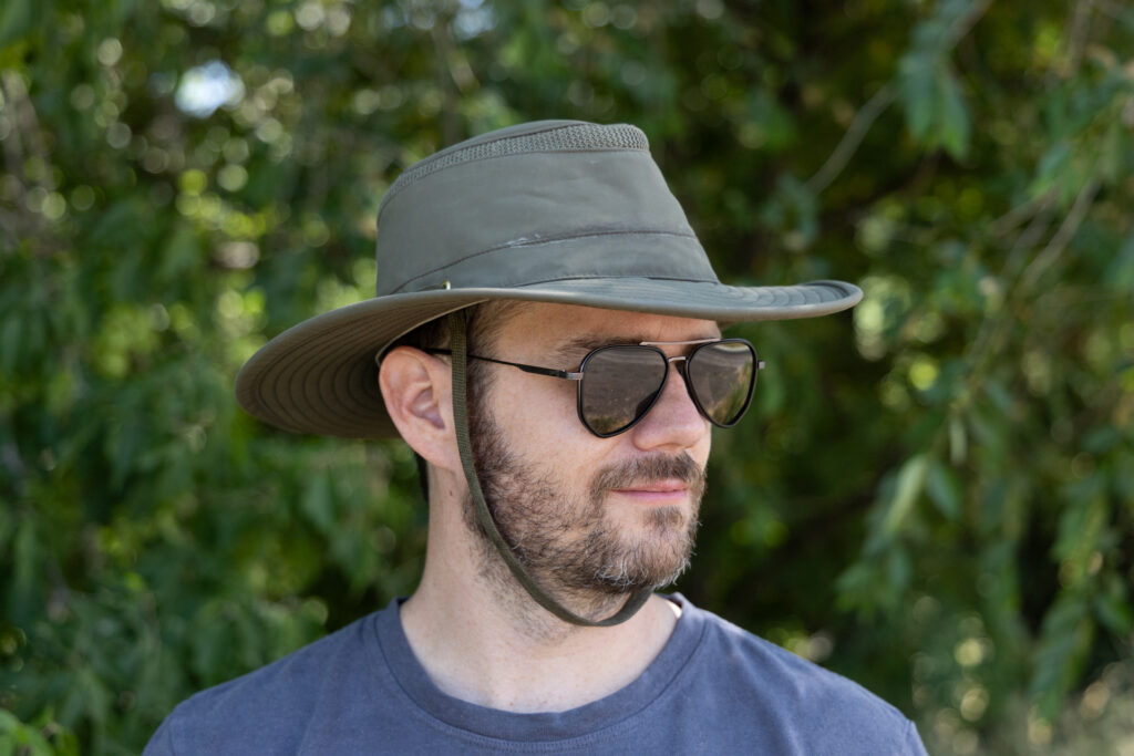 A man stands in the woods wearing a Tilley wide-brimmed AirFlo hiking hat.