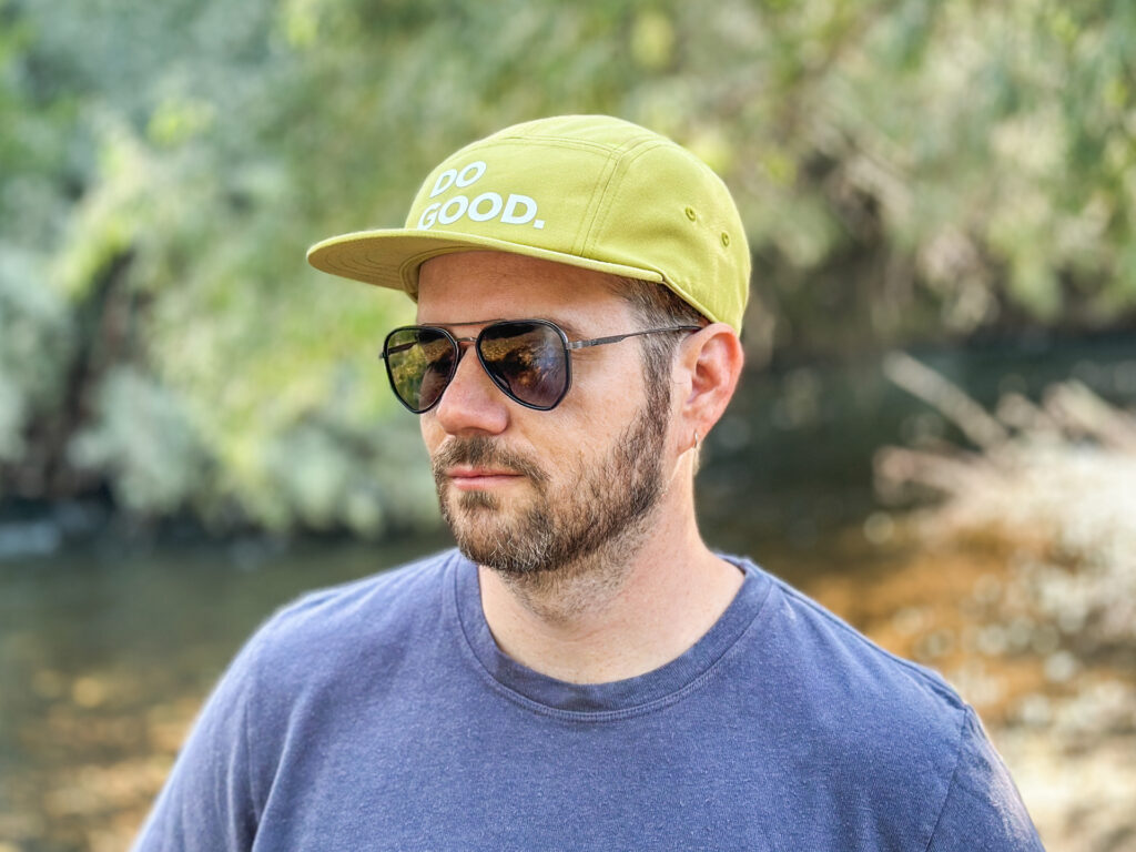 A man in sunglasses wears a green Cotopaxi 5-panel hat with the words "Do Good" on the front.