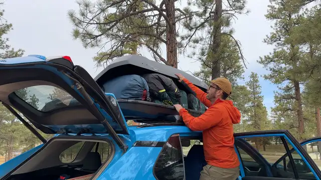A man packs camping gear into a Thule Force 3 rooftop cargo box.