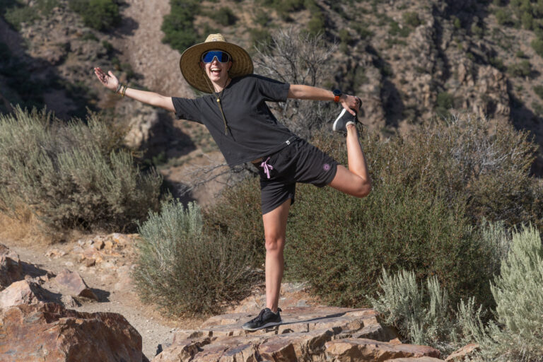 A woman does a silly yoga pose on desert rocks wearing Astral hemp tee and kinisi shorts.