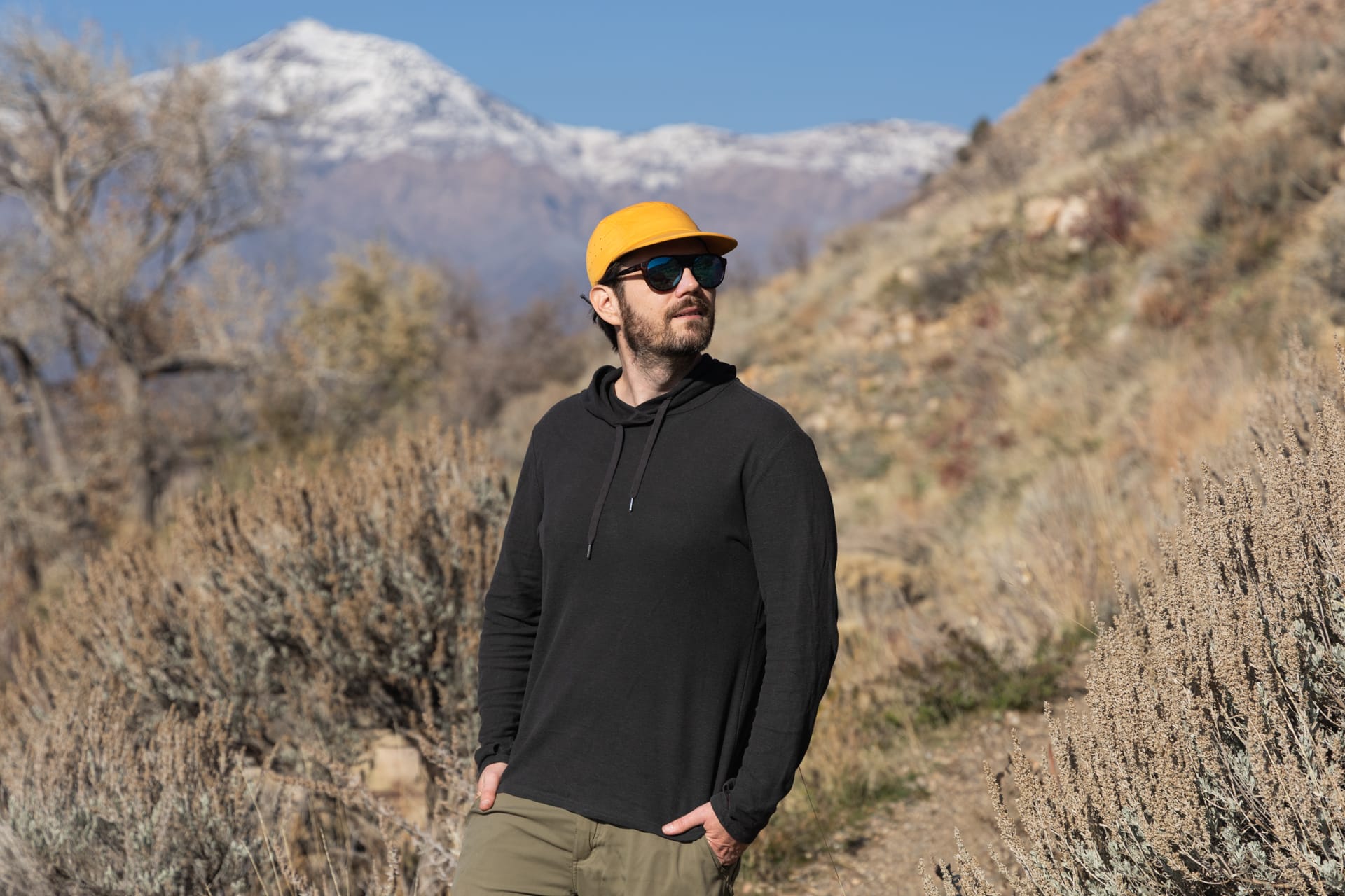 A man stands in front of a mountain on a trail wearing an Astral High Noon hemp hoodie.