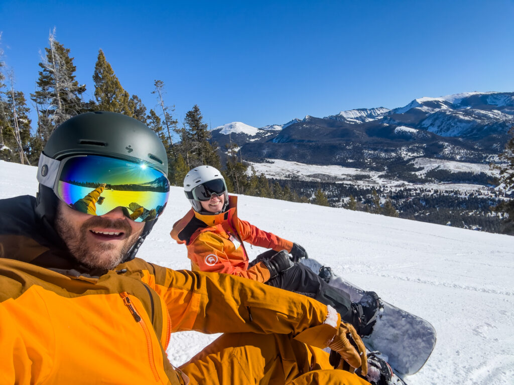 Two smiling snowboarders sit on the snow and take a selfie at Maverick Mountain Ski Resort in MT.