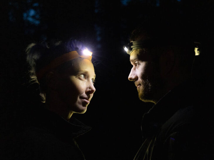 A man and woman look at each other, just their faces illuminated by headlamps.
