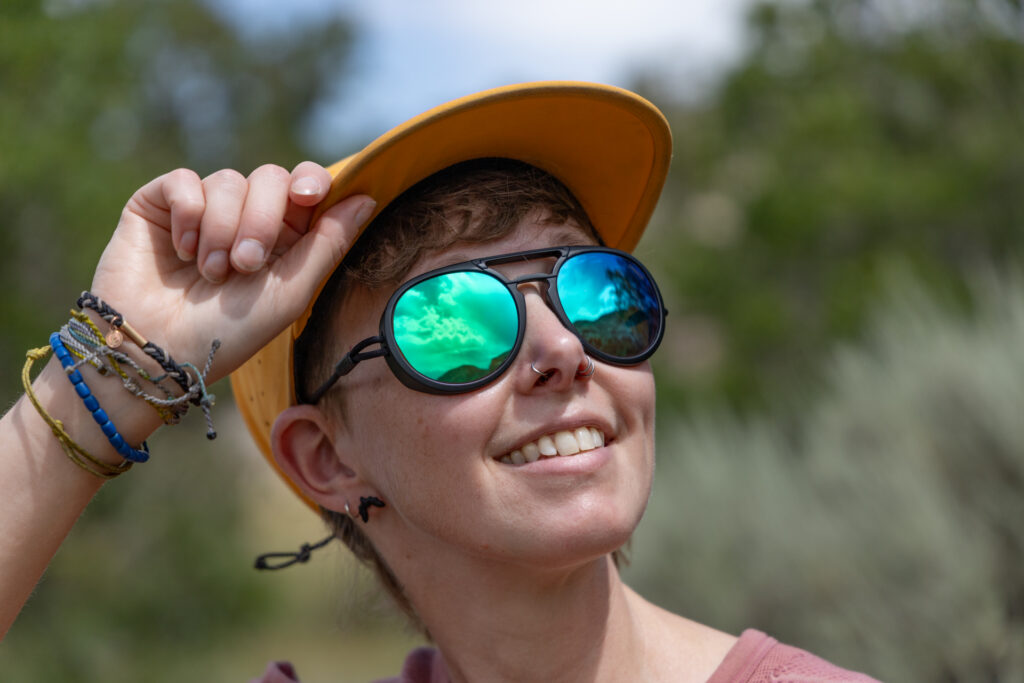 A woman in a hiking hat wears Ombraz Rx Viale armless sunglasses.