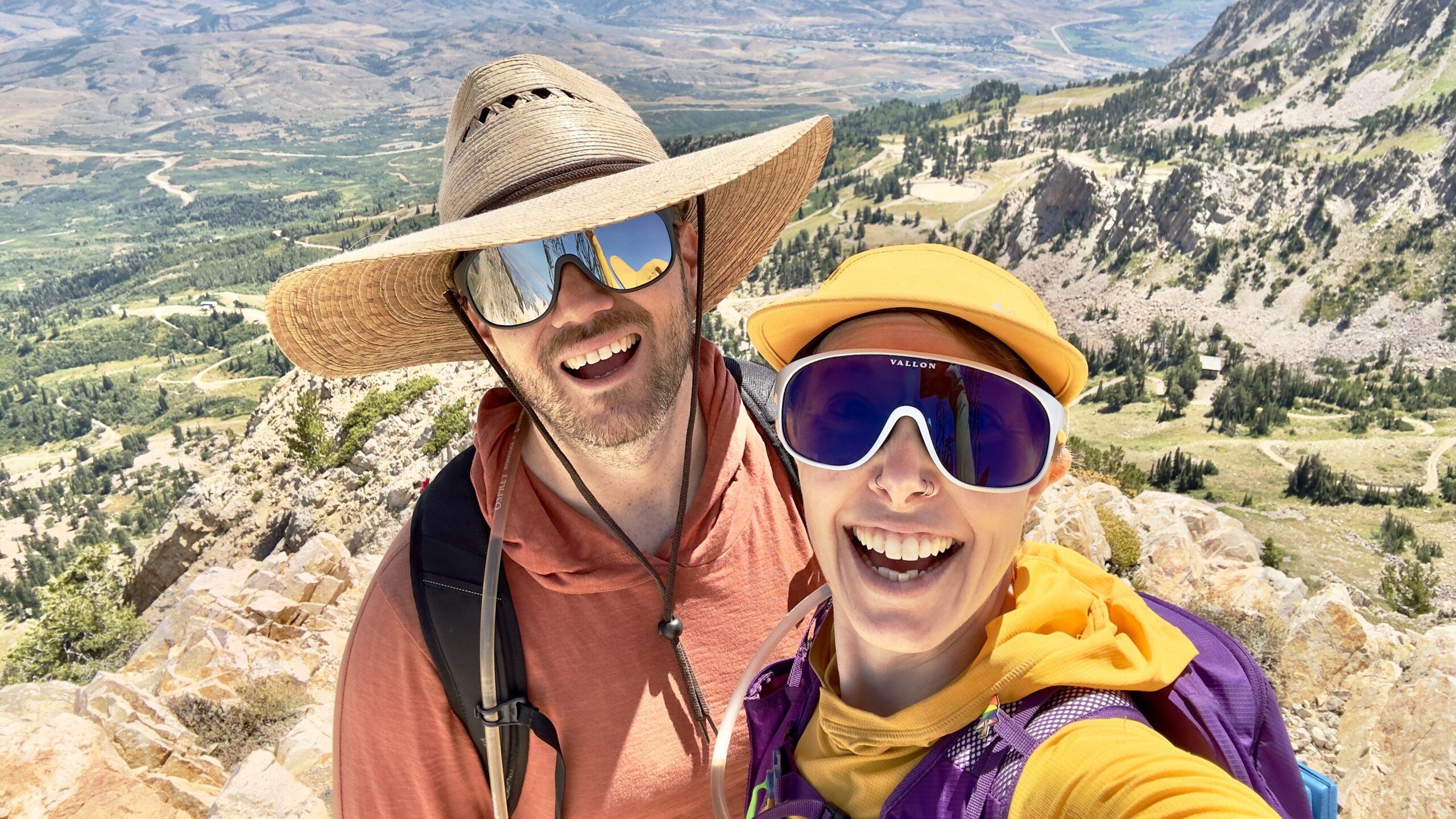 A man and woman wearing Vallon Watchtowers sunglasses smile on a mountain peak.