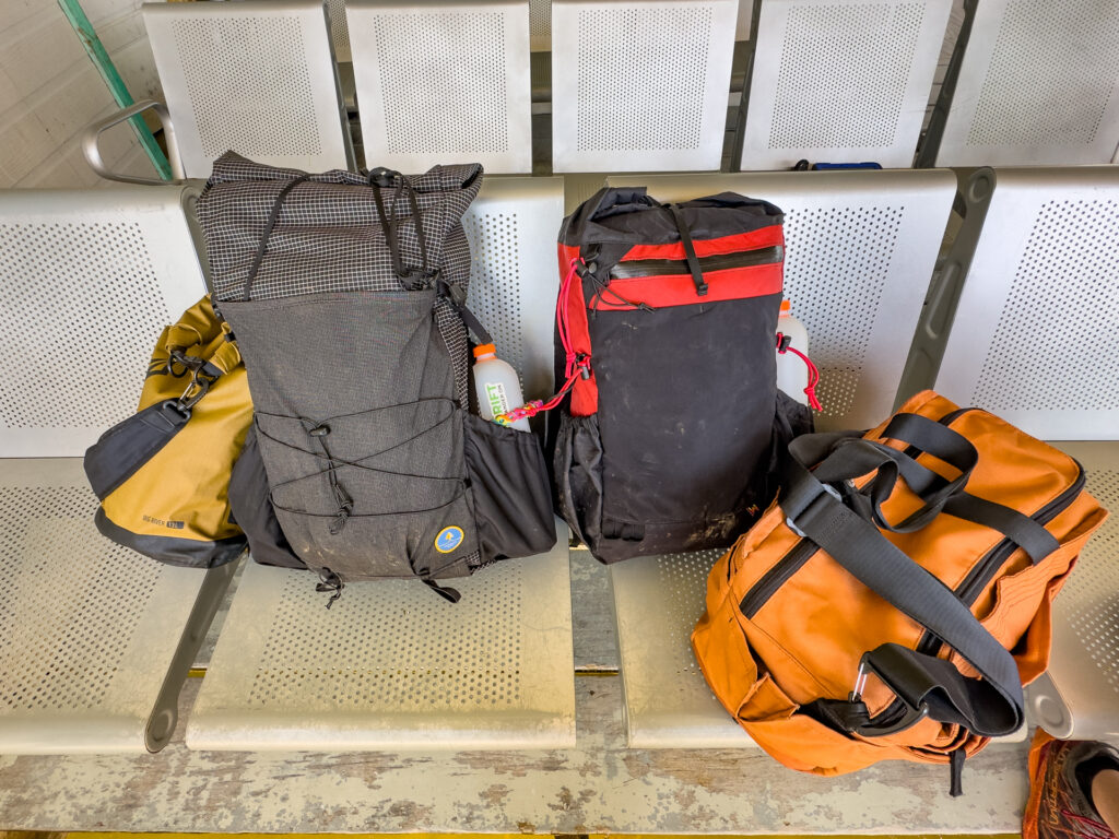 Two backpacks and a duffel and dry bag on terminal benches.