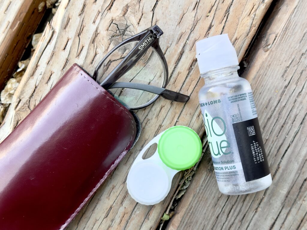 A pair of Smith glasses, case, contact case and travel bottle of contact solution on a table.