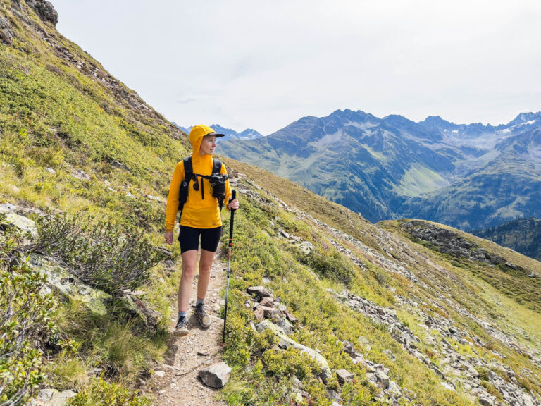 A woman stands on the trail with a backpack wearing an outdoor research echo sun hoodie.