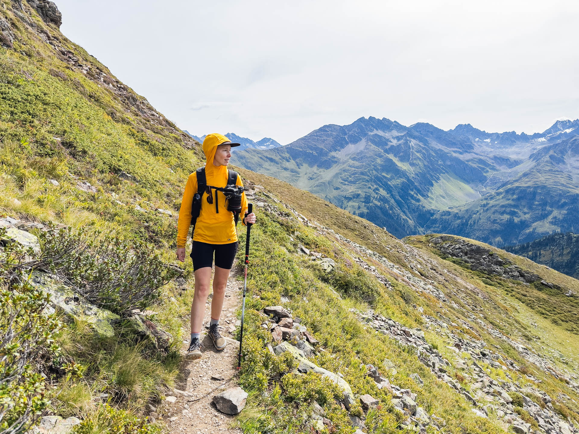 A woman stands on the trail with a backpack wearing an outdoor research echo sun hoodie.