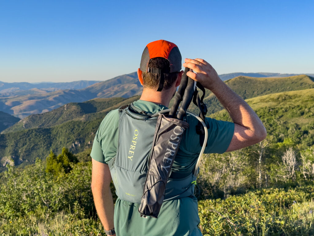 A man wears the Osprey Duro running hydration vest on a trail (rear view with quiver).