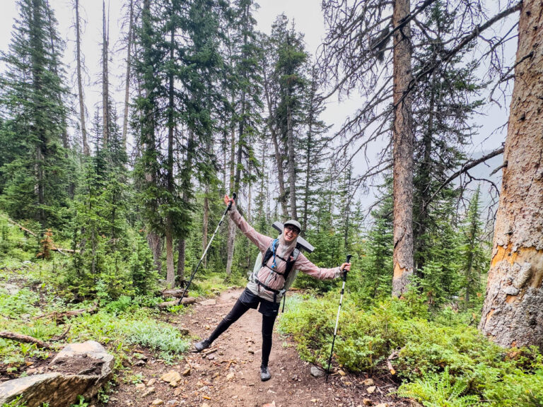 A woman hikes down a trail wearing a rain jacket and the Mountain Hardware Alakazam 45 ultralight backpack.