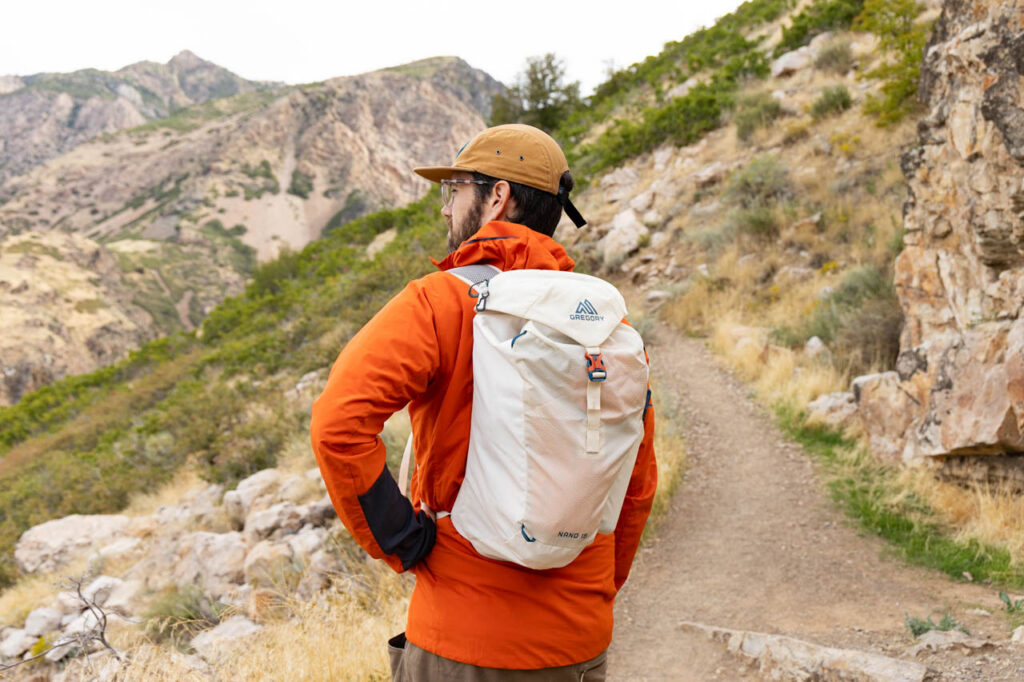 A man stands on a trail wearing a Gregory Nano 16 ultralight daypack.