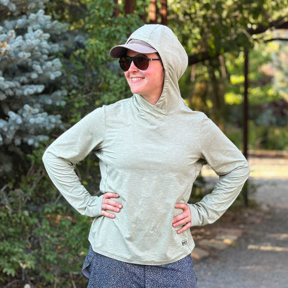 A woman wears the straight hem REI Co-op Sahara Shade Hoodie with a ball cap.
