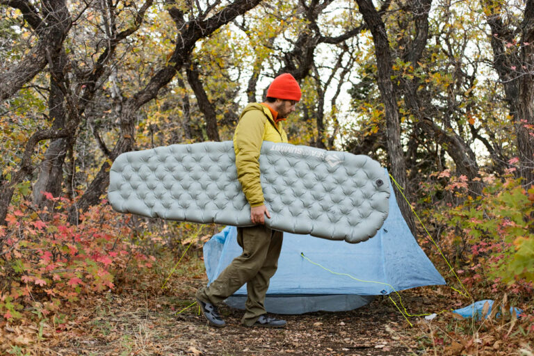 A man carries a Sea to Summit Ether Lite XR Sleeping pad through camp.